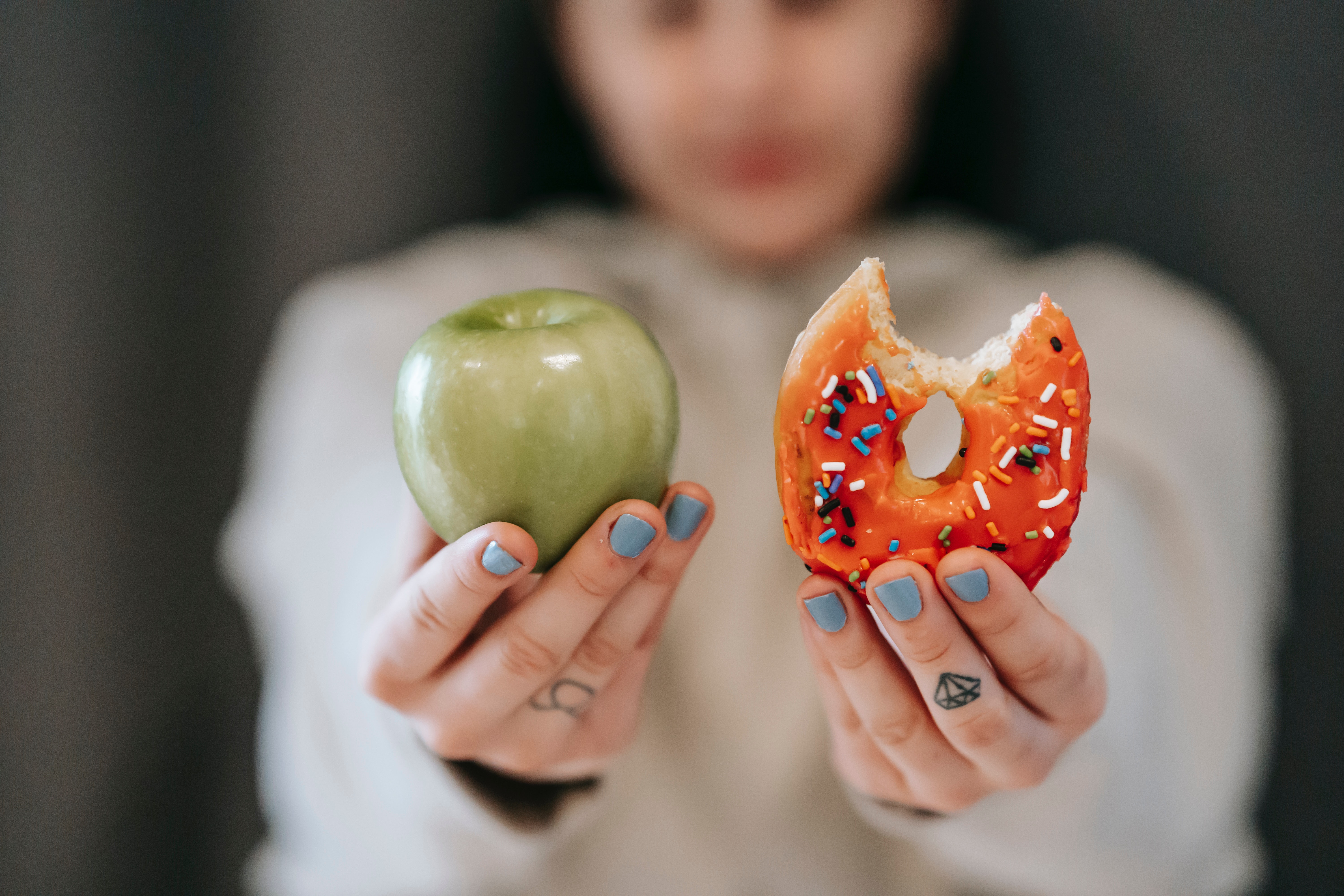 An employee who's physical wellbeing is tied to financial wellness holds a green apple and orange donut