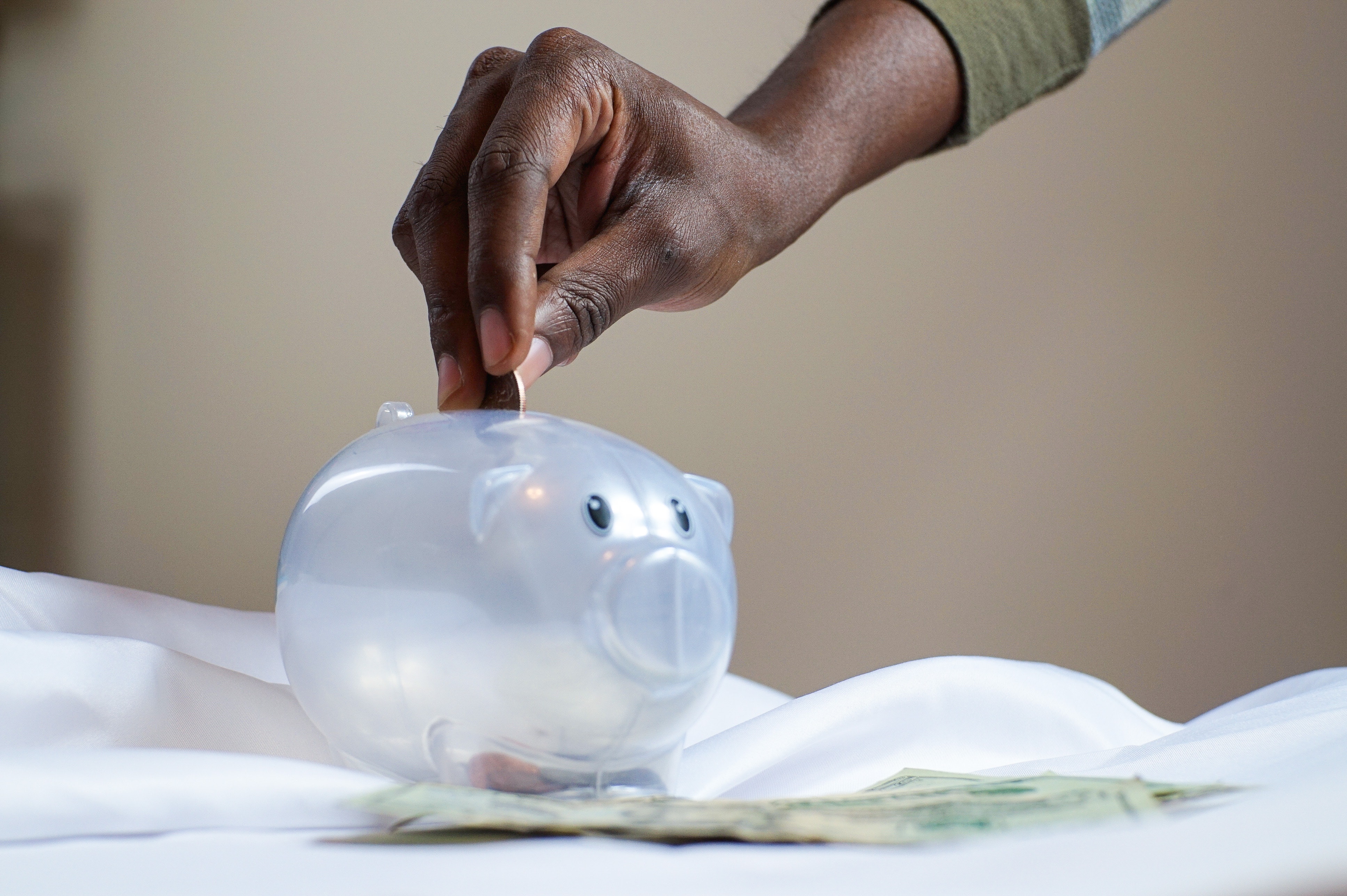 Hand places money into clear piggy bank to promote financial wellbeing
