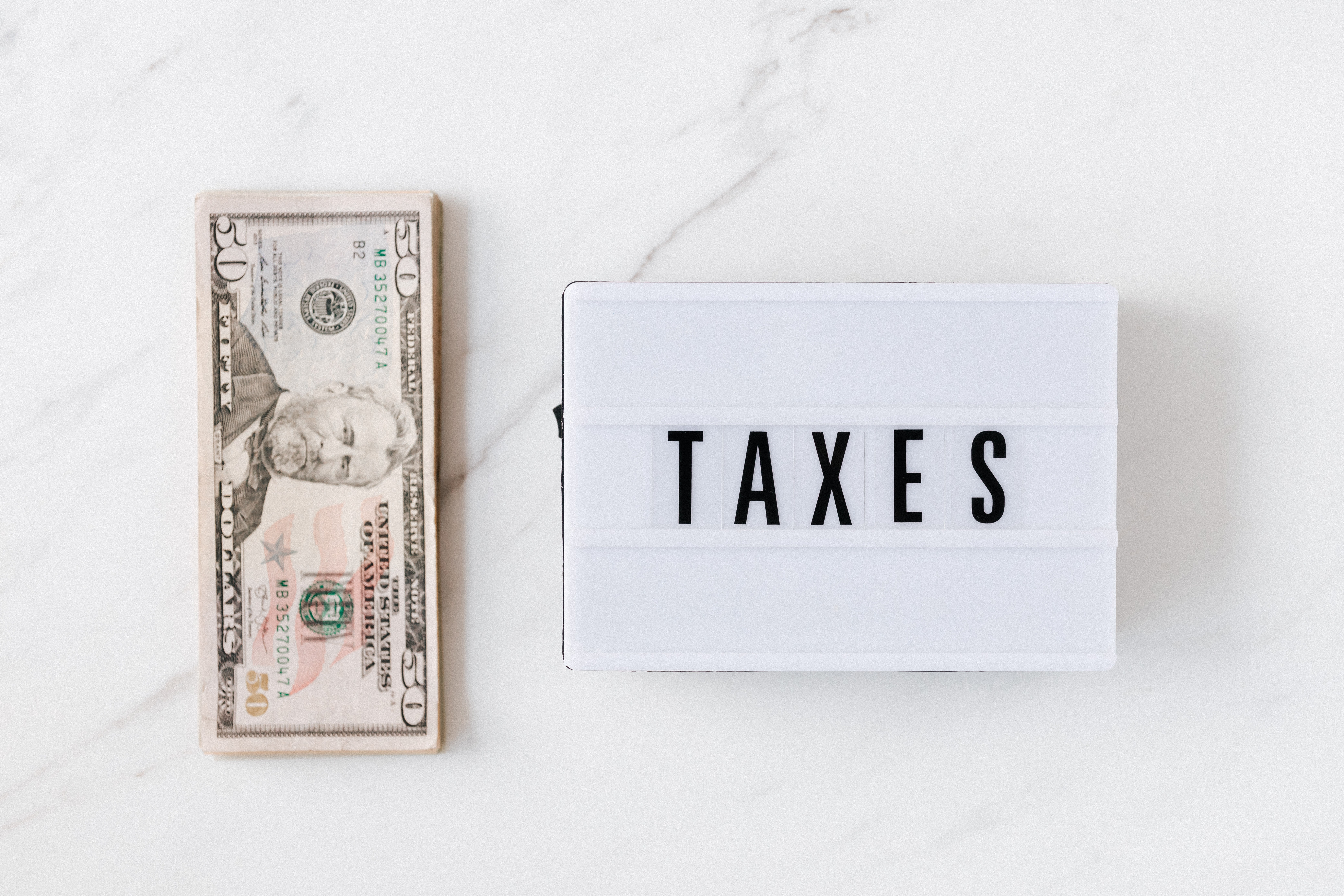 A stack of dollar bills next to a sign that says Taxes on white plastic
