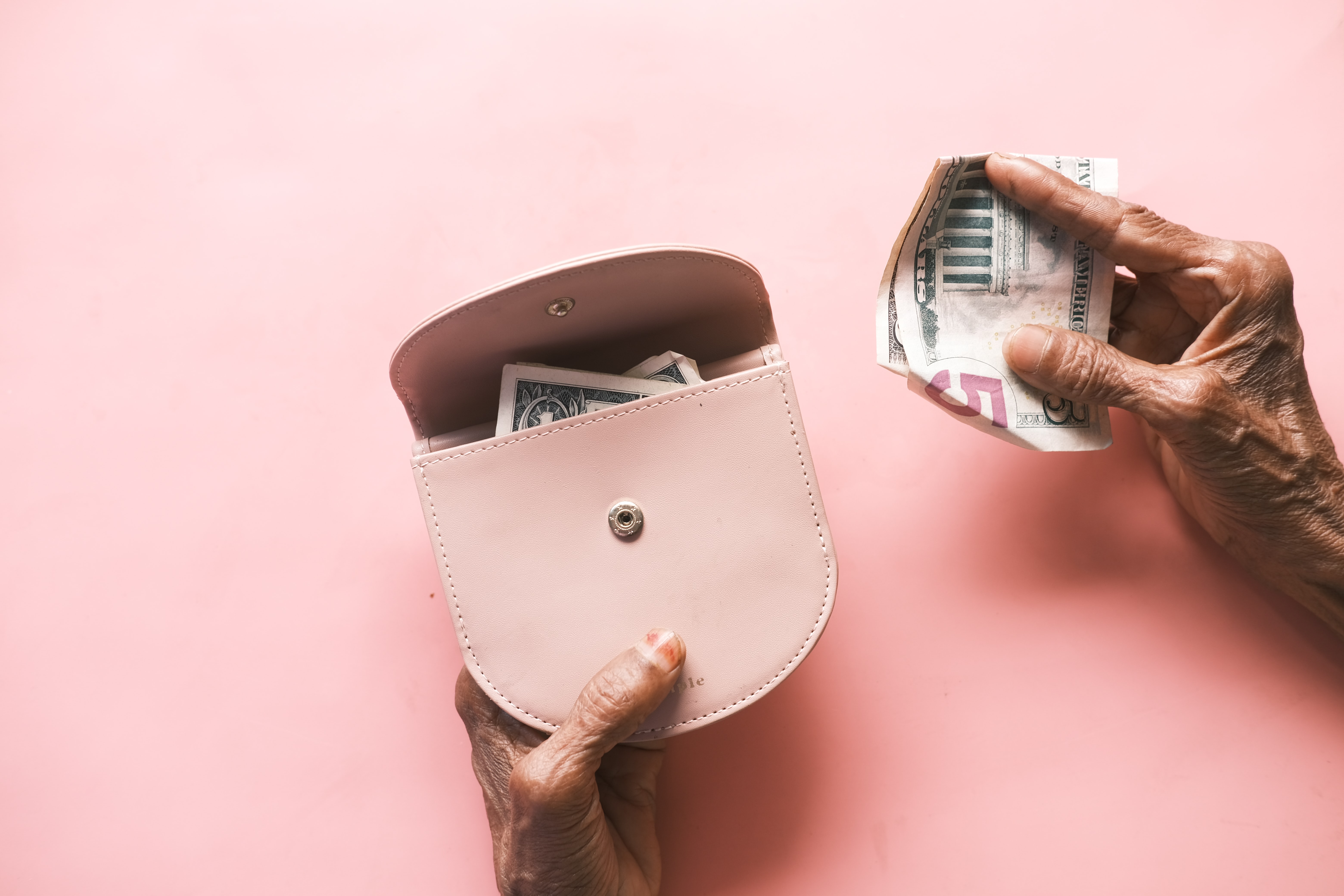 Woman's hand on pink background putting $5 into a pink purse for retirement